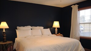 A neatly made bed with white linens in a room with dark walls, two bedside lamps, and a window with blinds. - Drive It Home Recent New Construction, 5 minutes to Dreams Park or Cooperstown (Cooperstown)