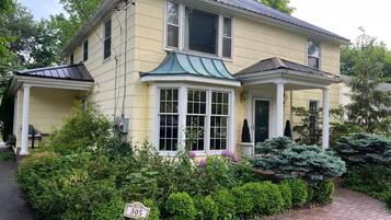 A two-story house with a wrap-around porch, a bay window, and a brick pathway leading to the entrance.
