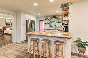 Une cuisine moderne avec un îlot central, des tabourets de bar, un réfrigérateur et des plantes en pot.