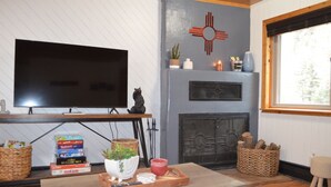 A living room with a flat-screen TV, a fireplace, and a window with a view of trees.