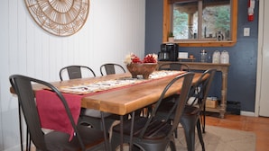 A dining area with a wooden table, black chairs, a red table runner, and a decorative wall piece.