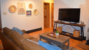 A living room with a brown leather sofa, a wooden coffee table, and a flat-screen TV on a stand.