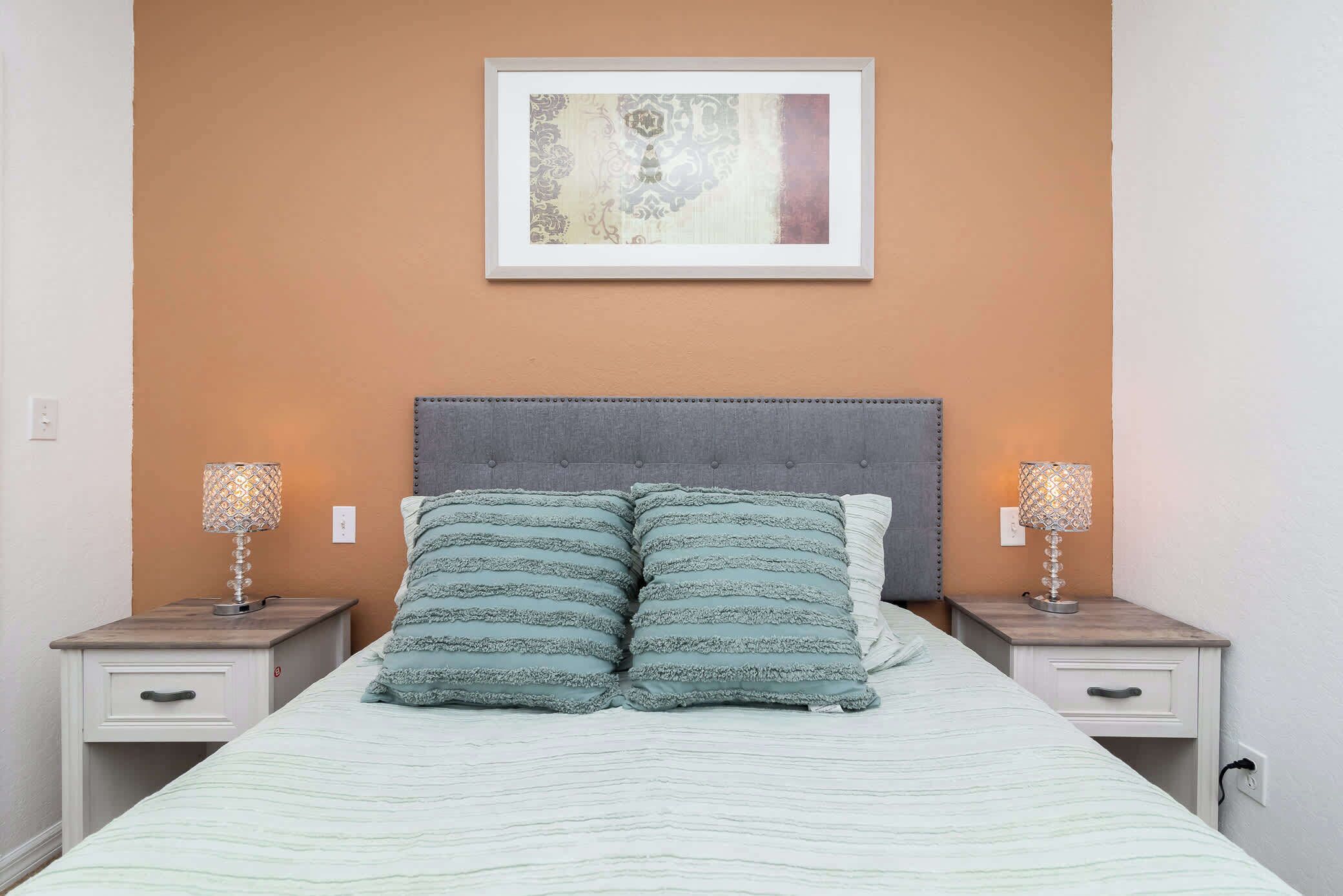 A neatly made bed with striped bedding, two bedside tables with lamps, and a framed artwork on the wall.