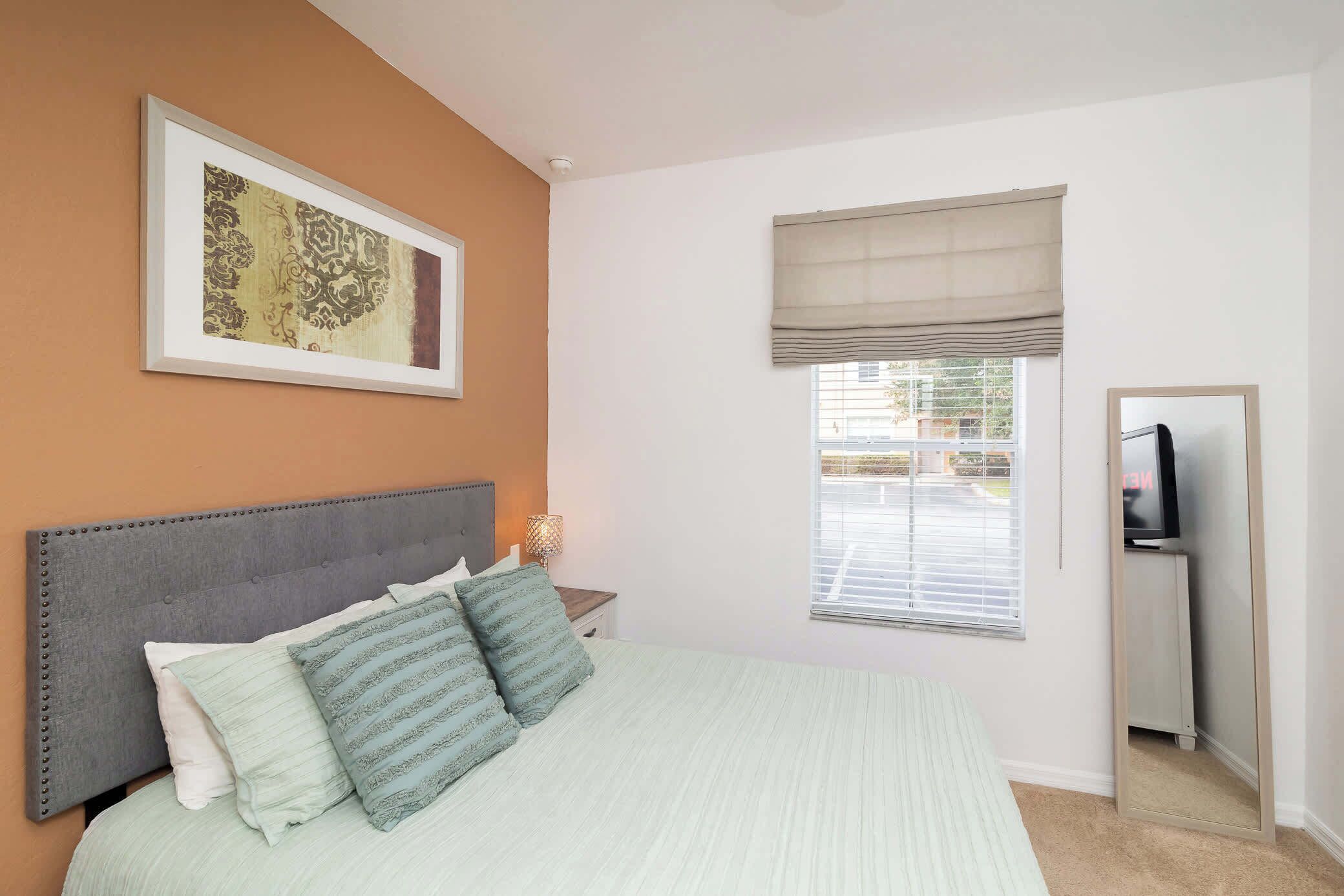 A bedroom with a bed, a nightstand, a television, and a window with blinds.