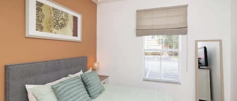 A bedroom with a bed, a nightstand, a television, and a window with blinds.
