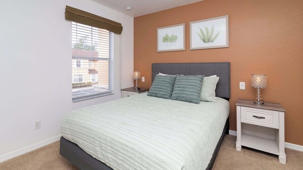 A bedroom with a bed, two bedside tables, a window with blinds, and two framed botanical prints on the wall. - Orlando's Heartland w/ Amenities (Kissimmee)