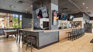 A modern bar area with a pool table, bar stools, and a counter with multiple screens displaying content.
