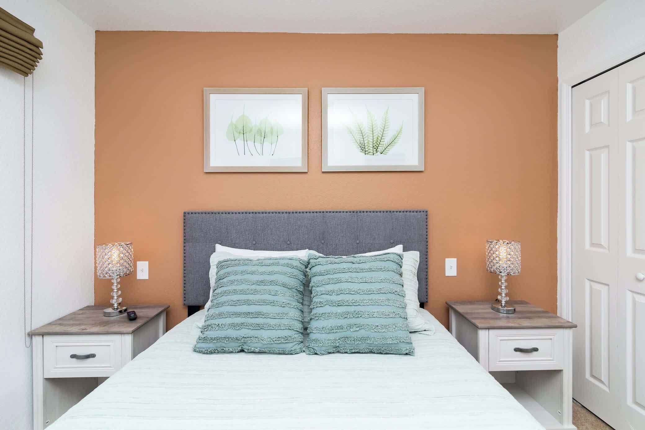A bedroom with a bed, two nightstands, a headboard, and two framed botanical prints on the wall.