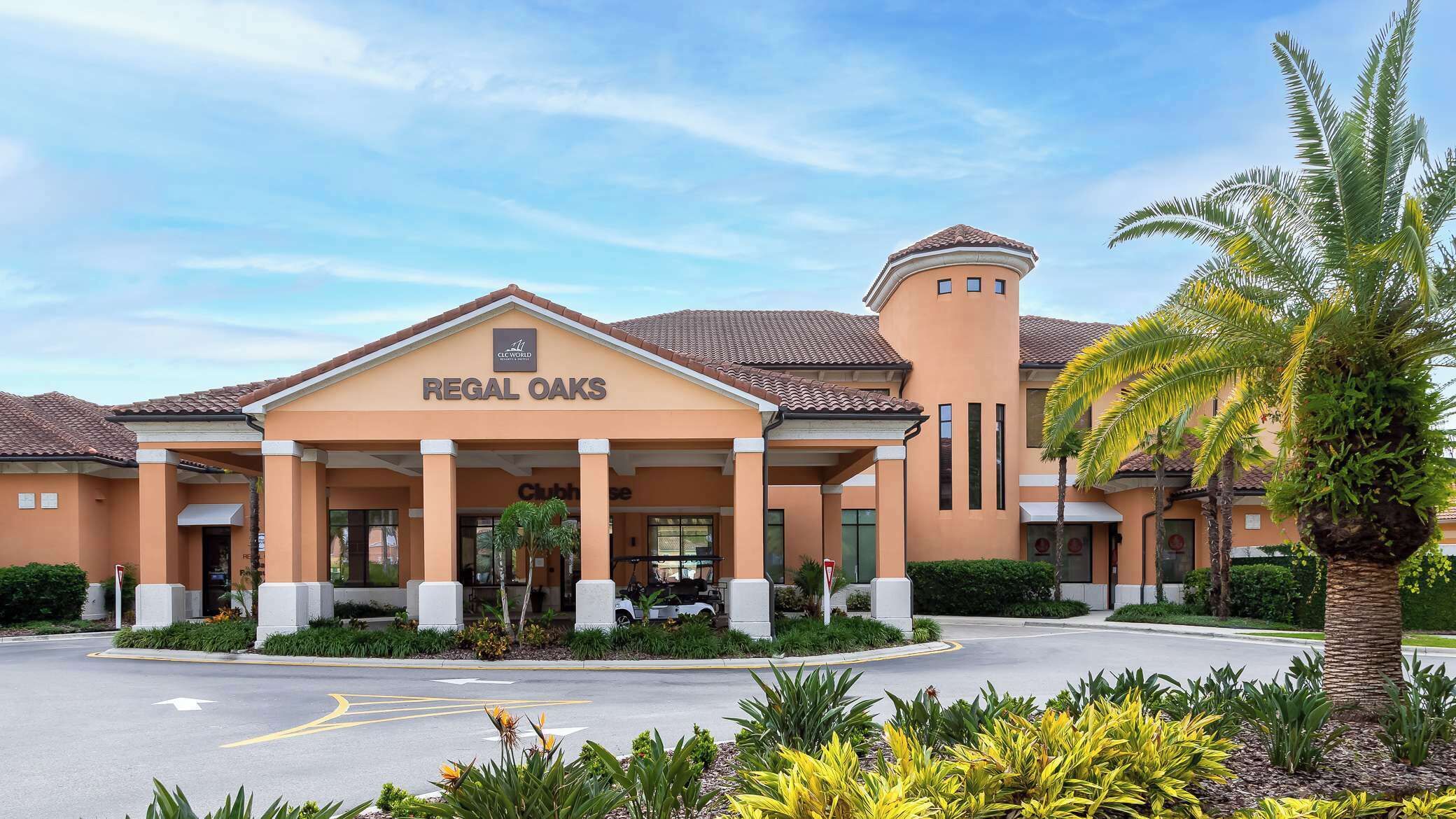 A hotel with a central entrance, a tower, and a landscaped area with palm trees.