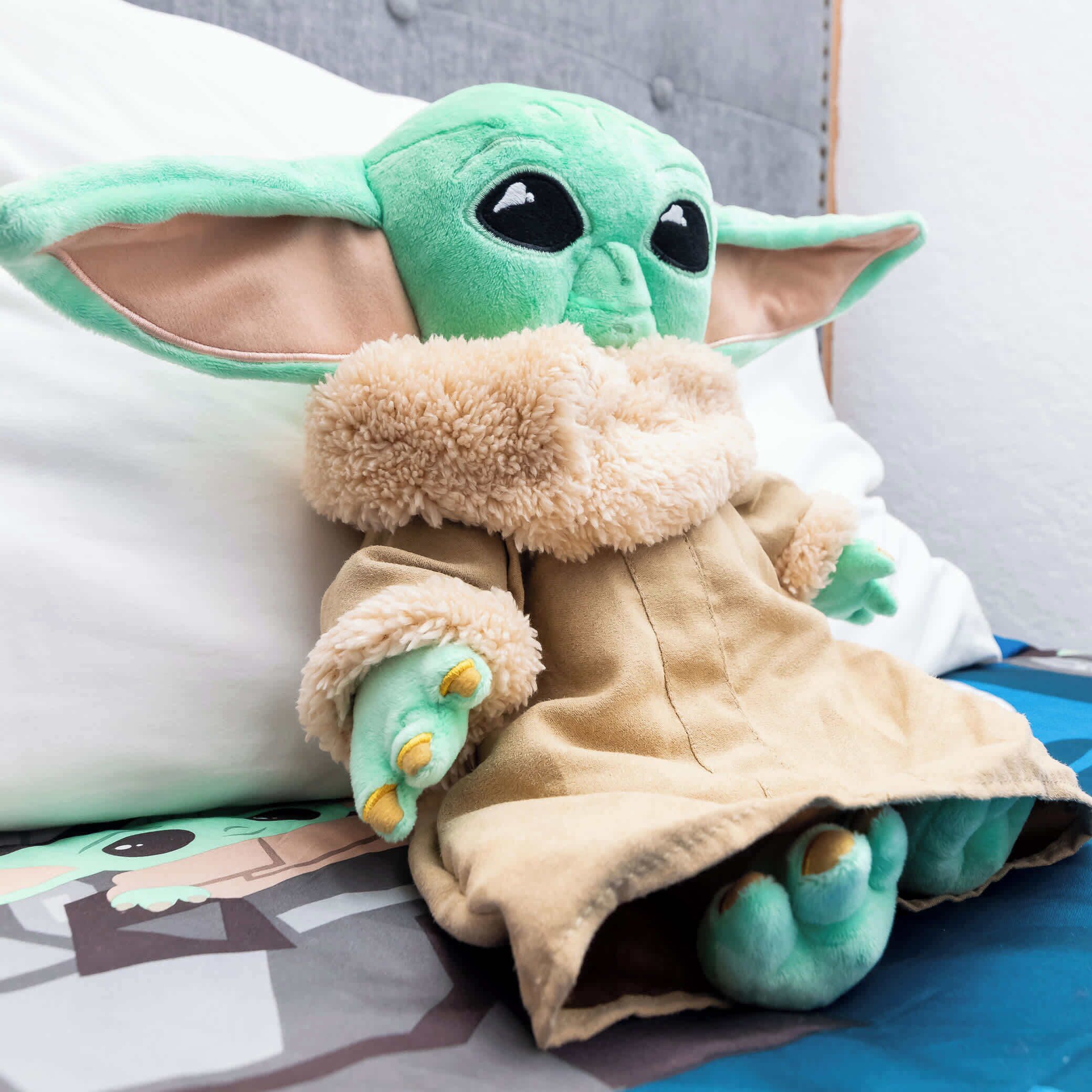 Un jouet en peluche représentant un personnage d’une série populaire, placé sur un lit recouvert d’une couverture à motifs.