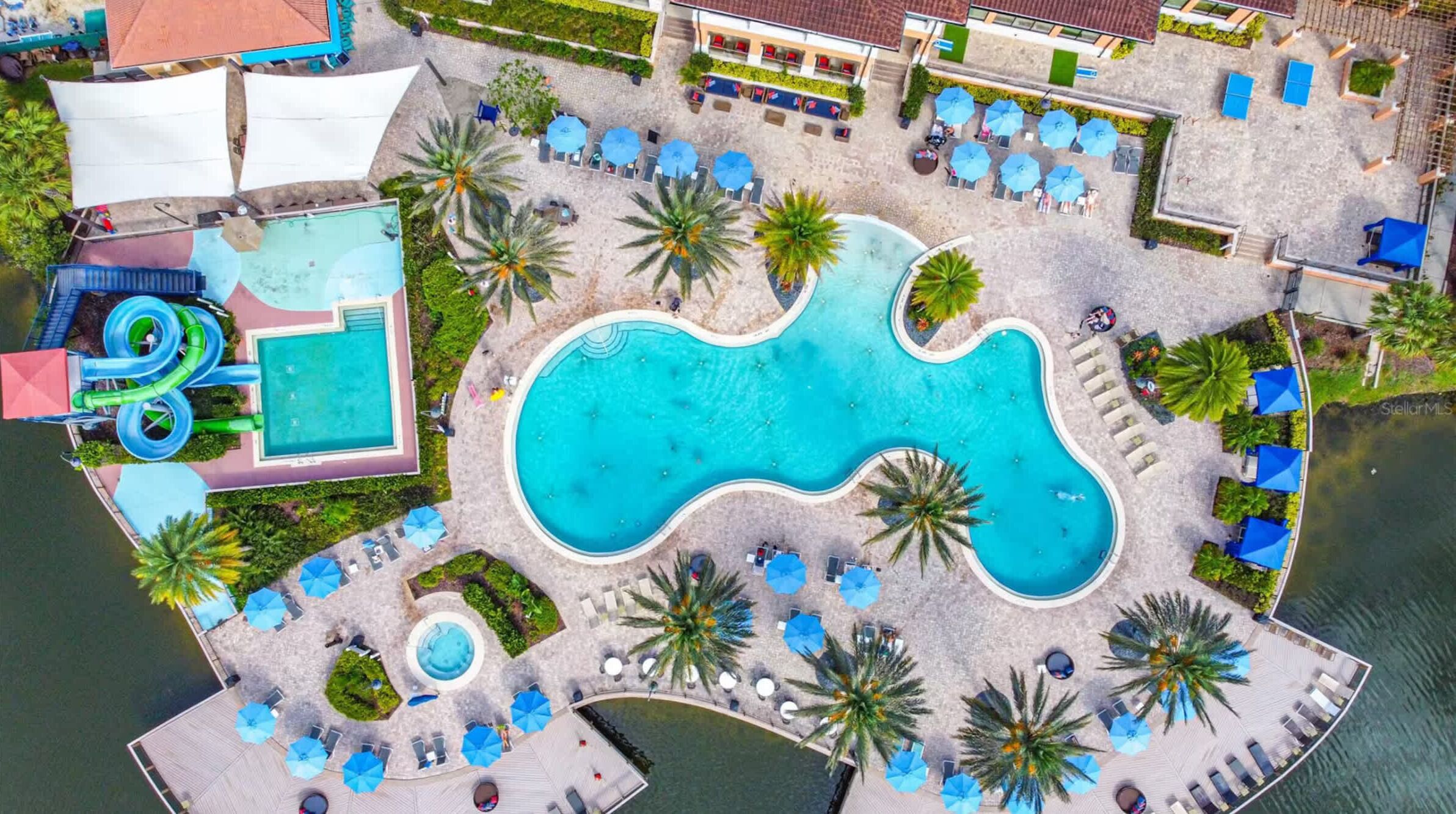 An aerial view of a resort with a large central pool, smaller satellite pools, and a water slide.