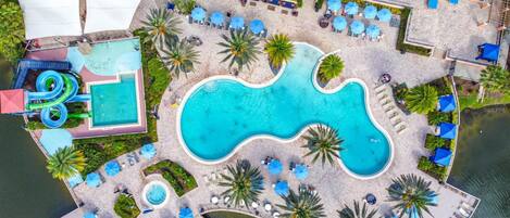 An aerial view of a resort with a large central pool, smaller satellite pools, and a water slide.