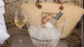 A wicker basket labeled "PRIVADO" with a wine bottle and ice, placed on a small table against a stone wall.