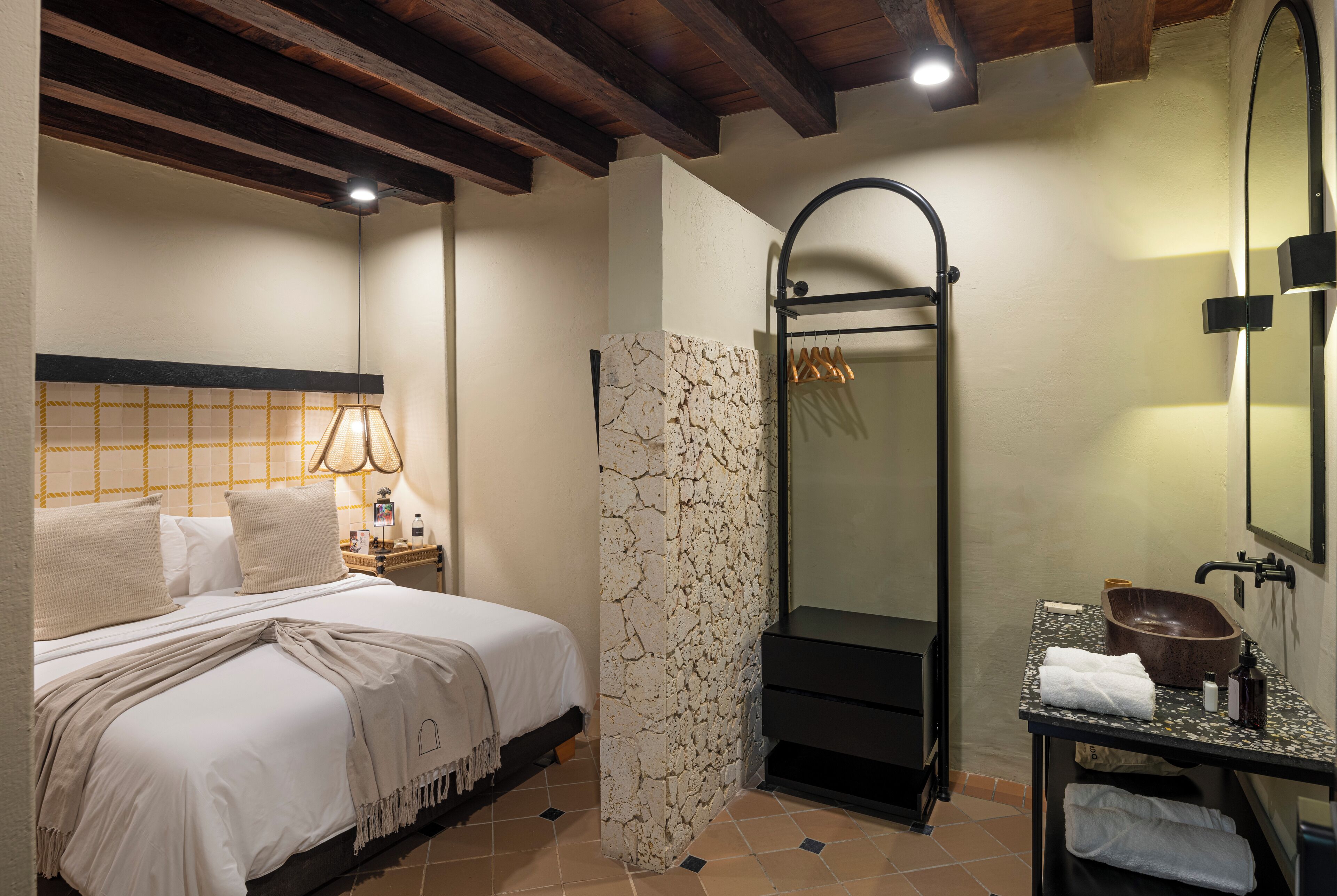 Een hotelkamer met een bed, een badkamer met een stenen muur, een spiegel en een wastafel.