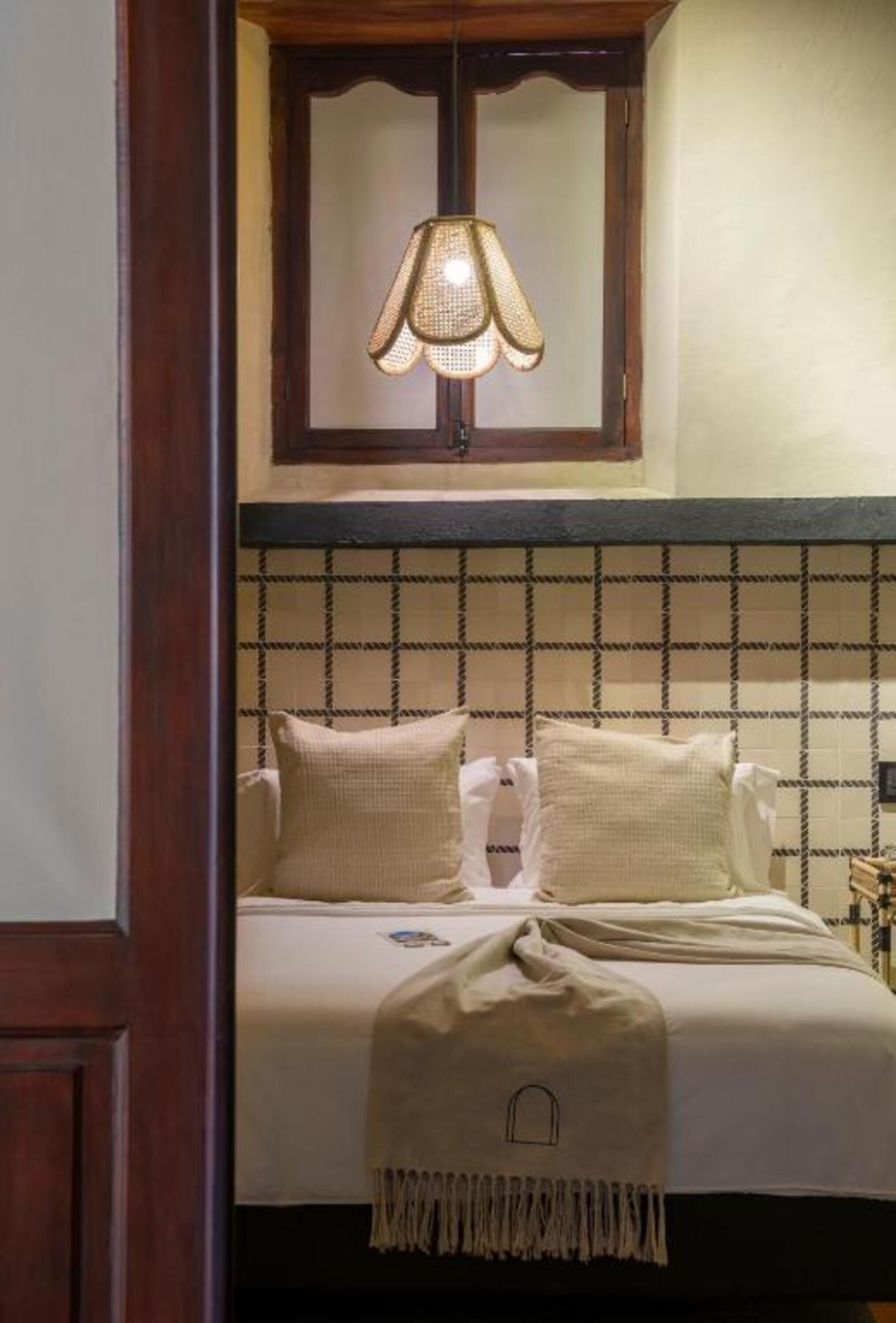 A bedroom with a bed, a window with a lamp, and a checkered headboard.