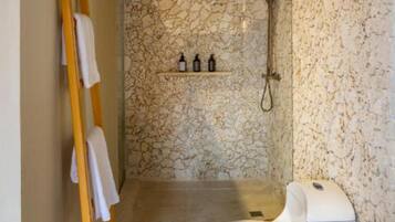 Un baño con pared de piedra, ducha, inodoro y escalera de madera.