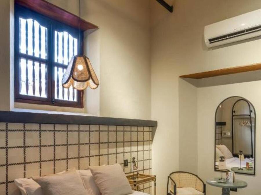 A bedroom with a bed, a window with a hanging light, a mirror, and a small table.