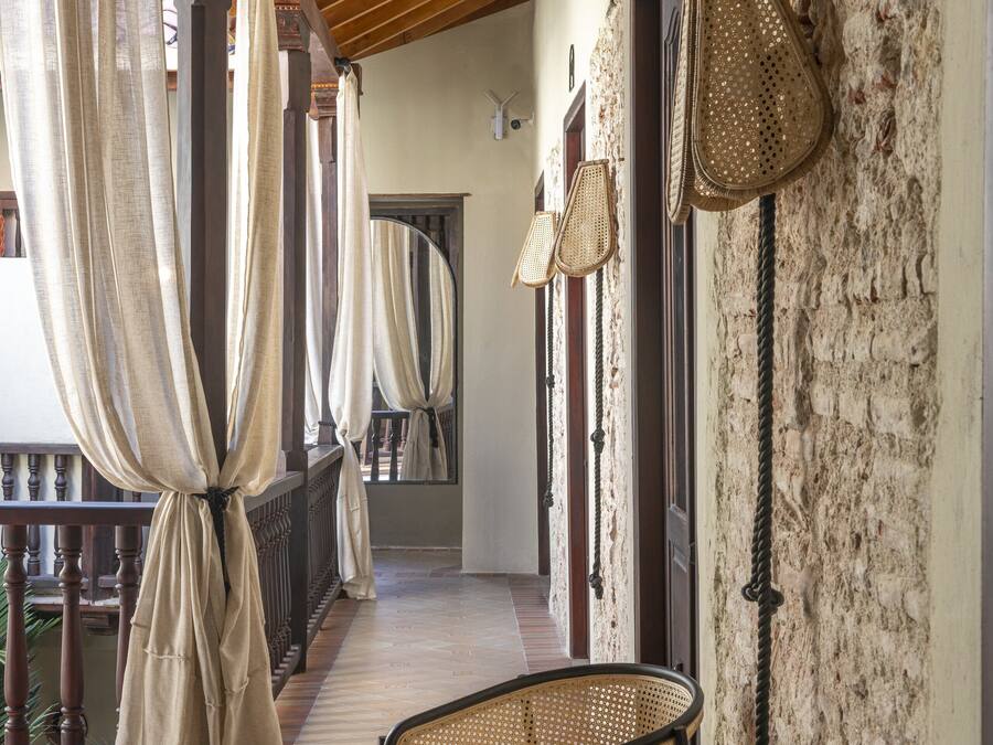 A corridor with wicker chairs, a wooden ceiling, and a stone wall.