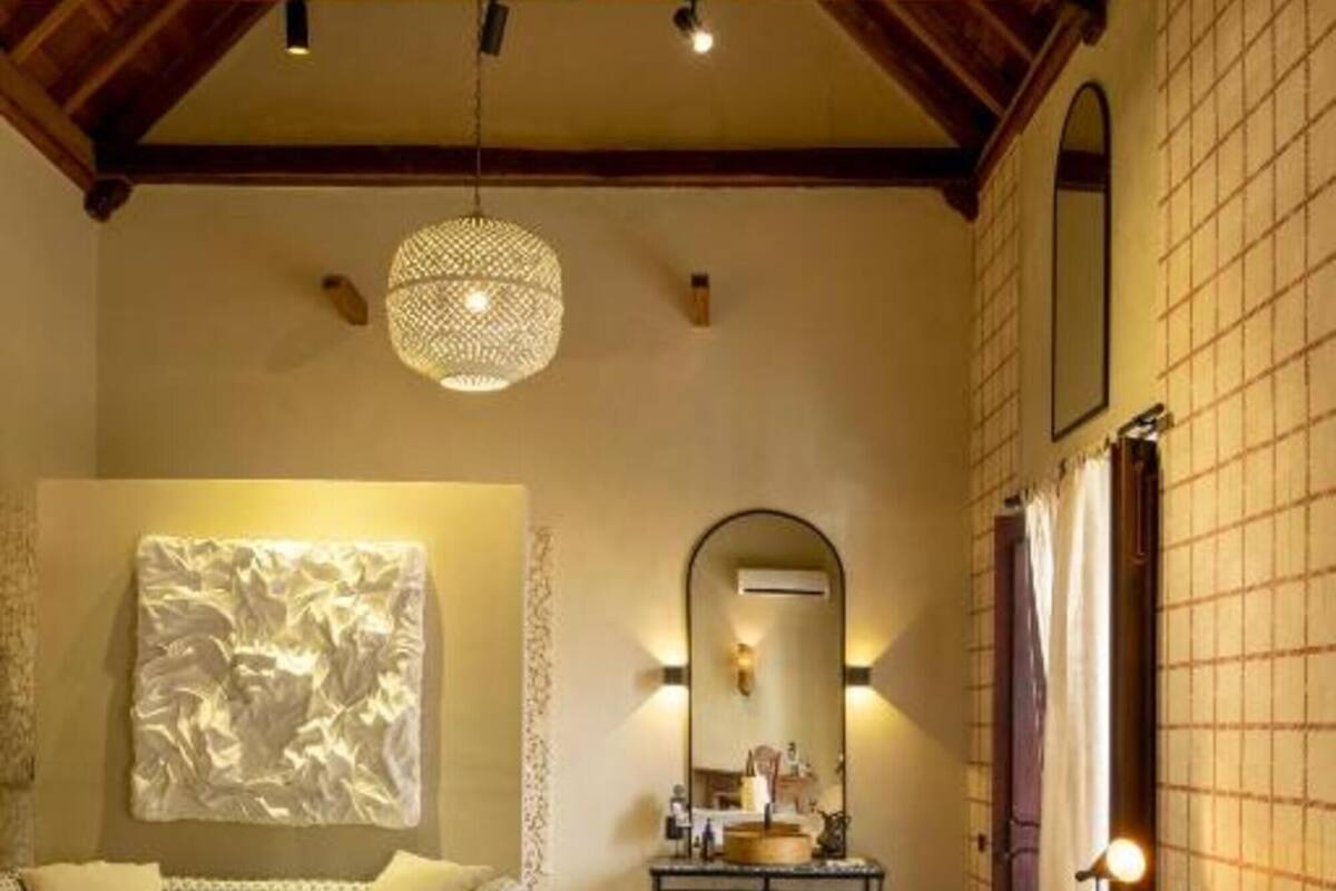 A bedroom with a large bed, a sofa, a side table, and a hanging light fixture.