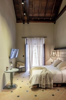 A bedroom with a bed, a TV, a chair, a table, and a window with curtains.