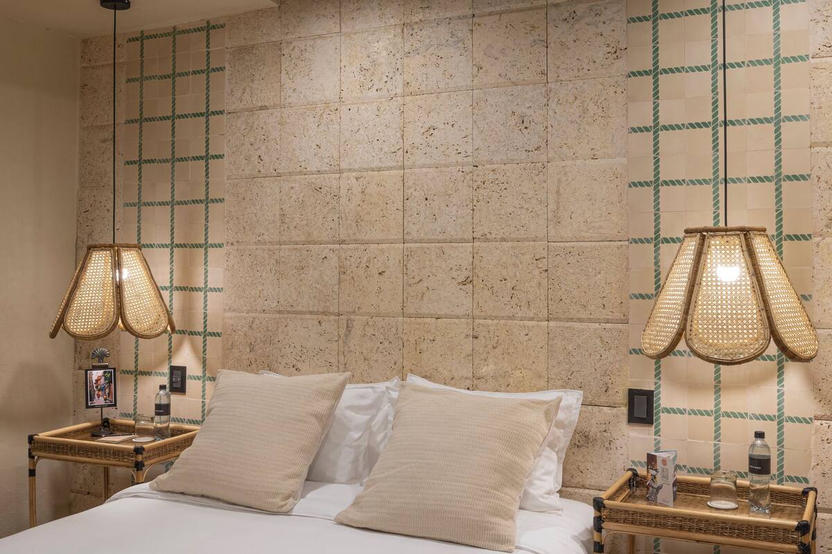 A bedroom with a large bed, two nightstands, two wall-mounted lamps, and a tiled wall with a green grid pattern.
