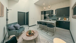 A modern kitchen with dark cabinets, a marble countertop, and a hanging light fixture. - Modern Suite ~ Above Starbucks ~ Fast Wi-fi (Logan)