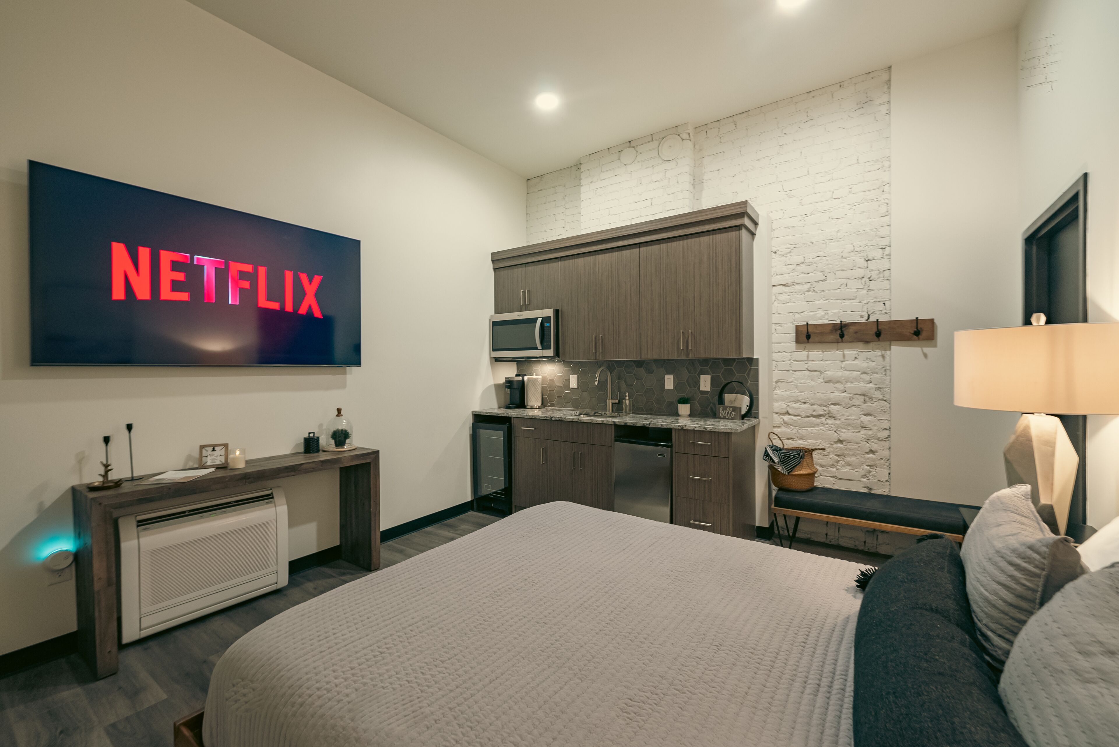 Ein modernes Schlafzimmer mit einem großen Bett, einem Fernseher mit dem Netflix-Logo, einer Küchenzeile mit einer Mikrowelle und einer Steinwand.