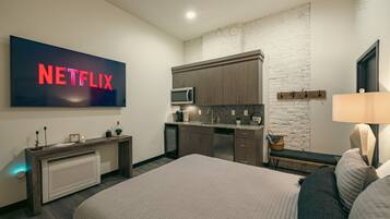 Ein modernes Schlafzimmer mit einem großen Bett, einem Fernseher mit dem Netflix-Logo, einer Küchenzeile mit einer Mikrowelle und einer Steinwand.