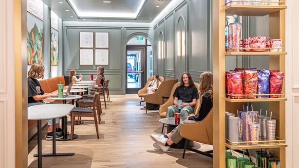 Un caffè moderno con posti a sedere, tra cui tavoli e sedie, e uno scaffale con diversi oggetti.