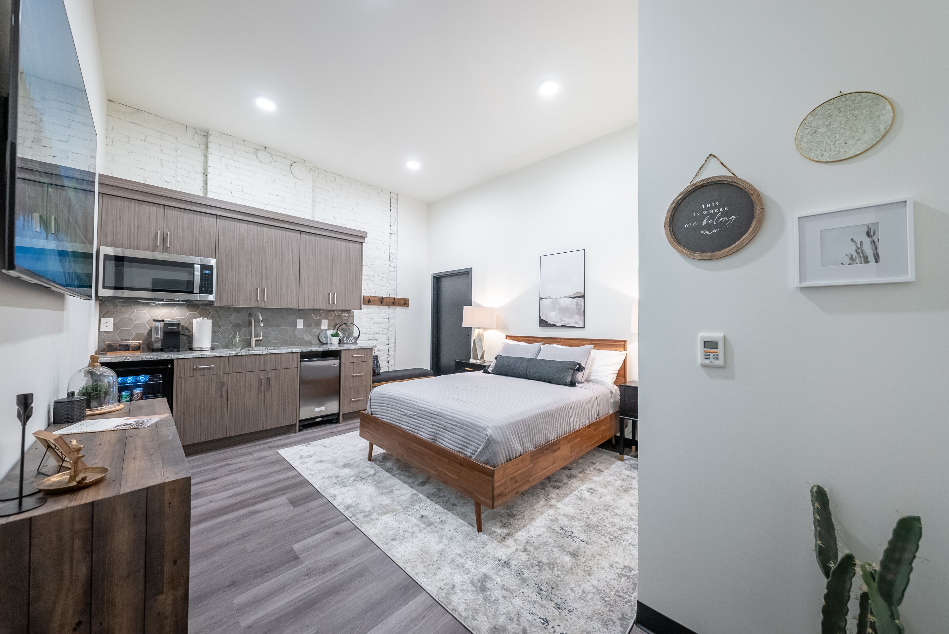 Une chambre moderne avec un lit, une table de chevet et une commode. Il y a également un coin cuisine équipé de placards, d’un four à micro-ondes et d’un évier.