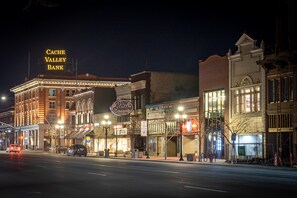 A street view at night with illuminated buildings, including a bank and a restaurant. - Luxury Suite ~ Above Starbucks ~ Main St View (Logan)