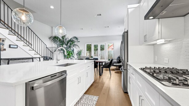 Une cuisine moderne avec des meubles blancs, un lave-vaisselle, une cuisinière à gaz et des luminaires suspendus.