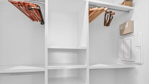 Une armoire blanche dotée de plusieurs étagères et d’un espace pour suspendre des vêtements, un mur blanc et un radiateur blanc.