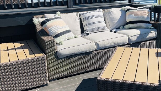 A covered outdoor seating area with a wicker sofa and two wooden tables.