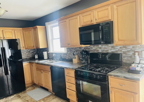 A modern kitchen with wooden cabinets, a black refrigerator, a microwave, a stove, and a dishwasher.