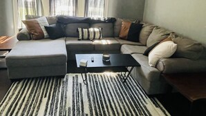 A modern living room with a sectional sofa, a coffee table, and a large window with sheer curtains.