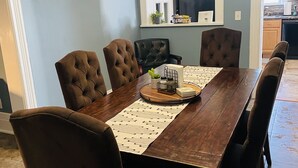 A dining room with a wooden table and six brown upholstered chairs.