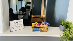 A dining area with a table and chairs, a sign with text, and snack bags on a shelf.