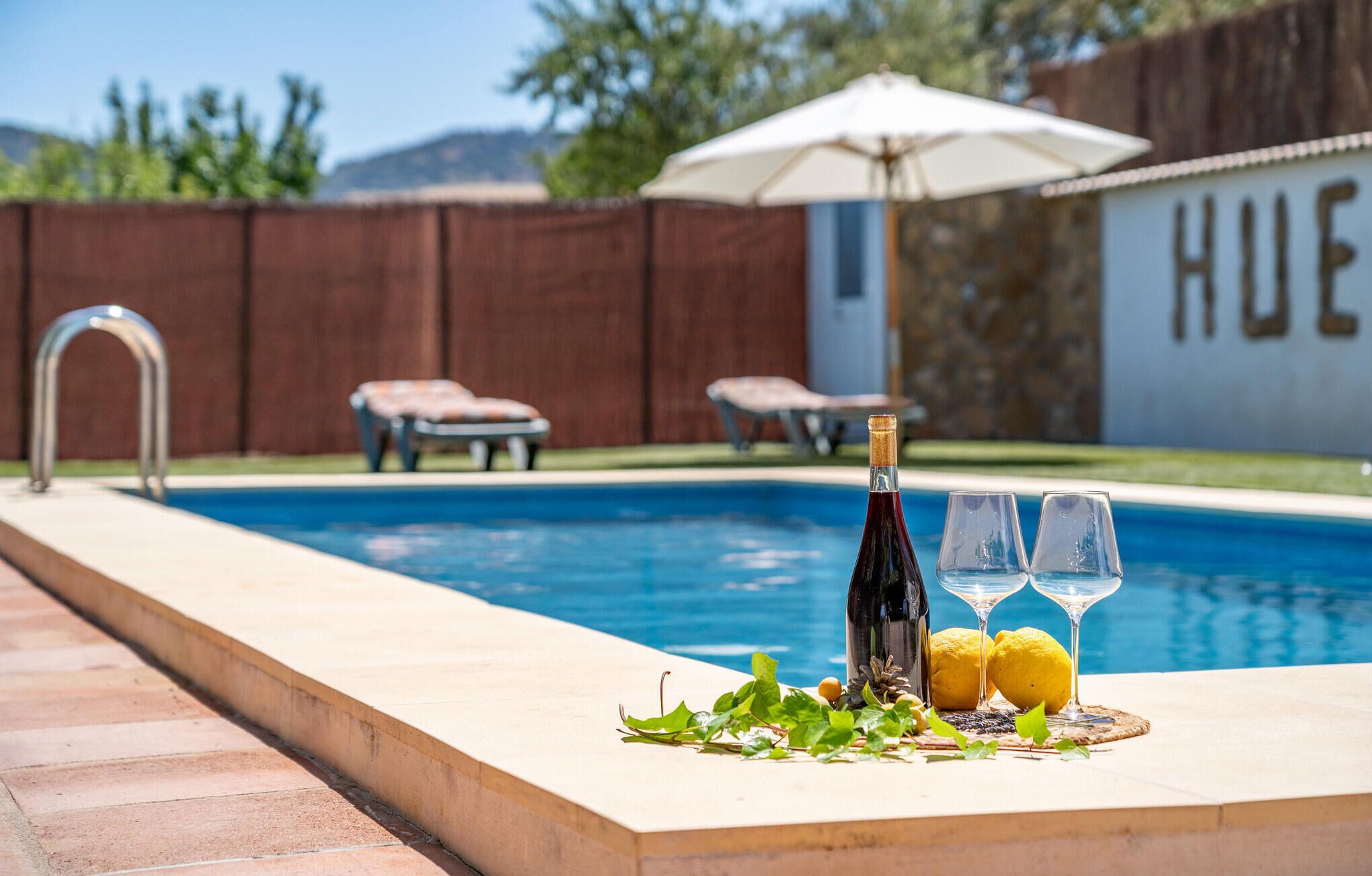 A pool area with a bottle of wine, two glasses, and lemons on the edge.