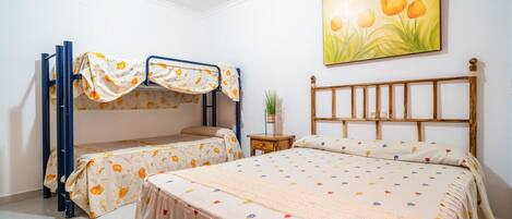 A bedroom with bunk beds, a single bed, a wooden headboard, a small bedside table, and a wall-mounted painting of flowers.