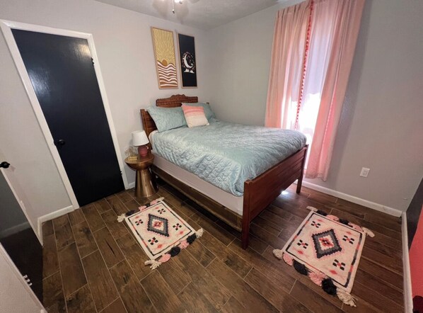 A bedroom with a bed, two rugs, a nightstand, and a wall with two framed pictures. - 5 minutes from winery! Spacious home with pool & hot tub! (Saint Jo)
