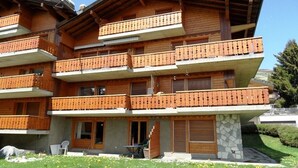 Ein mehrstöckiges Holzgebäude mit Balkonen, einem Steinsockel und einem Rasen vor der Fassade.