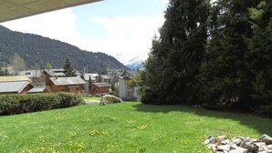 Eine grüne Rasenfläche mit einer Steinmauer, einer Holzhütte und einem Berg im Hintergrund.