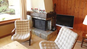 Ein gemütliches Wohnzimmer mit Kamin, zwei Polstersesseln, einem Flachbildfernseher und einer Holzvertäfelung.