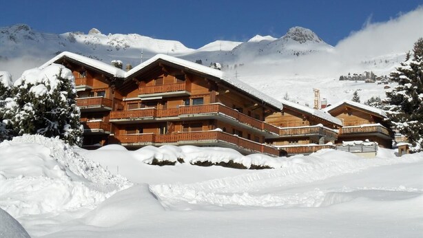 Eine Holzchalet mit mehreren Balkonen, umgeben von schneebedeckten Bergen.
