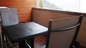 A balcony with a wooden wall, a black table, and a chair.