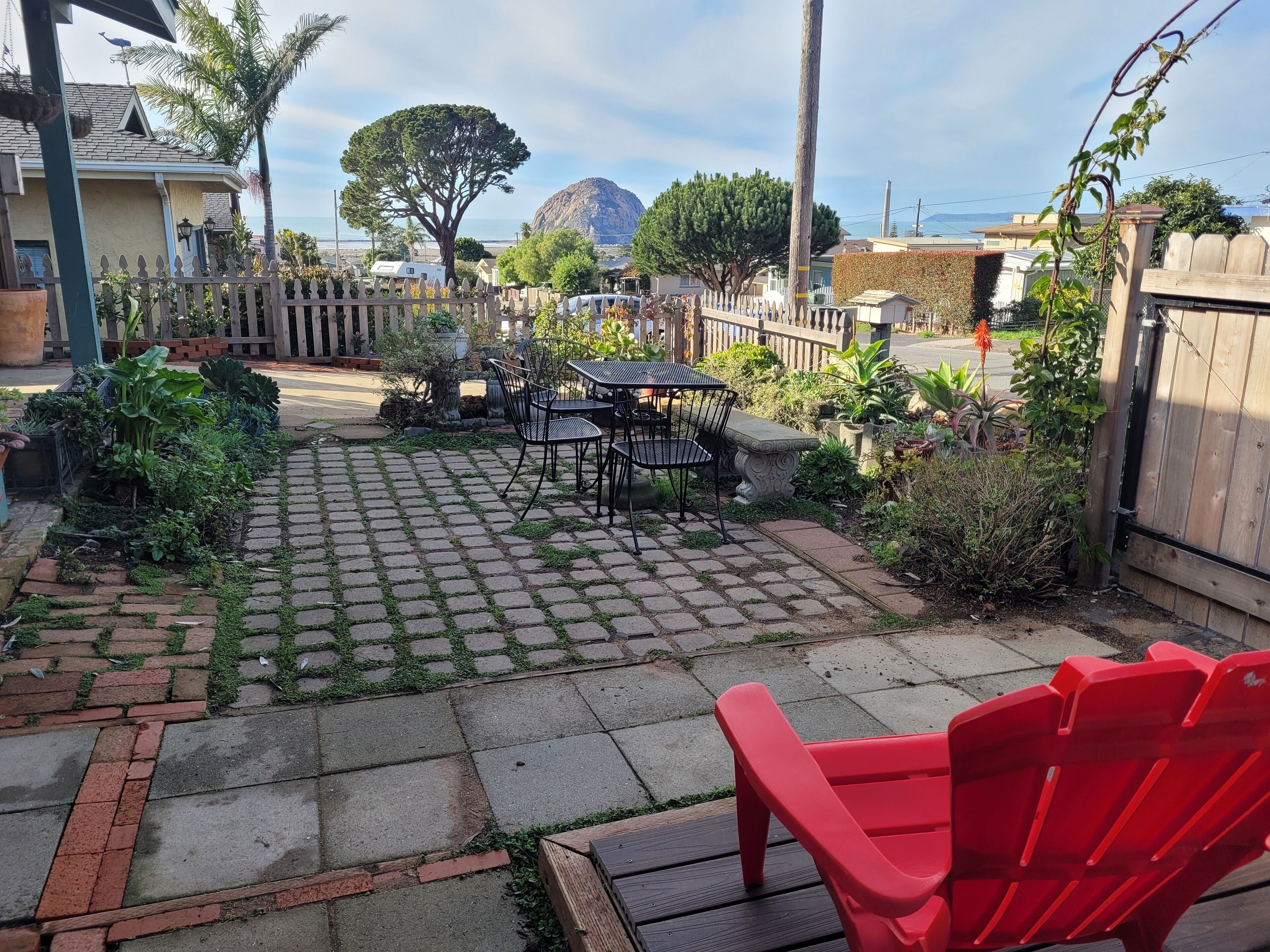 A backyard patio with a table and chairs, surrounded by potted plants and a wooden fence.