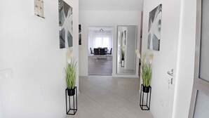 Un couloir aux murs blancs, un coin repas à l’arrière-plan et deux plantes en pot de chaque côté.