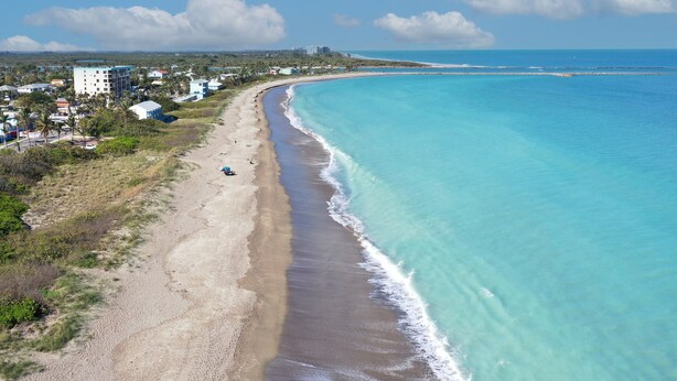 An aerial view of a beach with a clear blue ocean, a sandy shore, and buildings in the background. - Thumb Point Oasis w/Heated Pool- walk to beach! (Fort Pierce)
