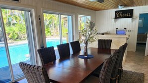 A dining area with a wooden table, wicker chairs, and a view of a swimming pool. - Thumb Point Oasis w/Heated Pool- walk to beach! (Fort Pierce)